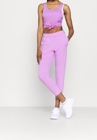 Pink sports tank top with a knotted detail paired with matching pink stretch pants. Smooth fabric, fitted design, and elastic waistband. White sneakers.