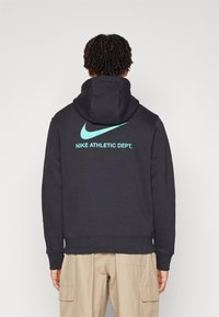 Haut à capuche bleu marine foncé avec un grand logo Nike bleu clair et le texte "NIKE ATHLETIC DEPT." au dos. Comprend une poche kangourou et un cordon de serrage pour la capuche.