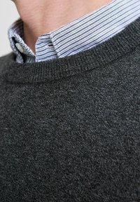 Gros plan sur un pull en tricot gris porté par-dessus un col de chemise à rayures blanches et bleues.