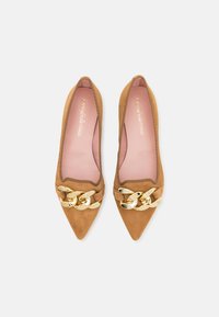 Ballerines pointues en suede beige avec un accent en chaîne dorée sur le devant. La doublure rose pâle et la texture lisse rehaussent le design.