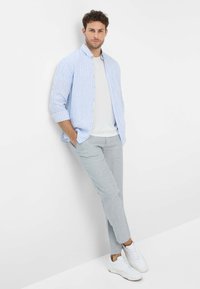 Light blue and white striped button-up shirt, white t-shirt underneath, grey pants, and white sneakers. Appears casual and modern.