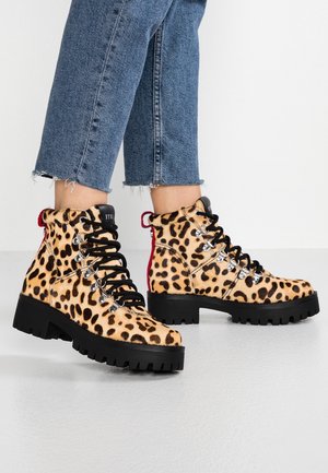 Bottines à imprimé léopard avec lacets noirs et œillets en métal argenté, semelle en caoutchouc, présentant un accent rouge au talon et une finition en fourrure texturée.
