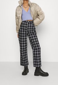 Beige vadderad jacka, ljuslila kort topp, svart och vit rutiga högmidjade byxor och svarta klumpiga ankelstövlar.