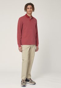Polo a maniche lunghe rossa con colletto e colletto interno a contrasto. Indossato con pantaloni cargo beige e sneakers con accenti grigi e blu navy.