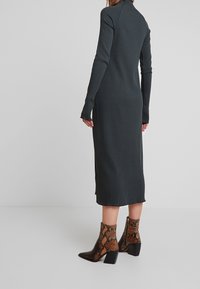 Robe midi côtelée, gris foncé, avec des manches longues et un col haut. Associée à des bottines à talon carré en imprimé serpent marron.