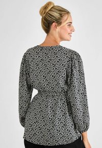 Schwarze und weiße gemusterte Bluse mit Puffärmeln, taillierter Passform und runder Ausschnitt. Der Stoff wirkt leicht und hat eine dezente Textur.
