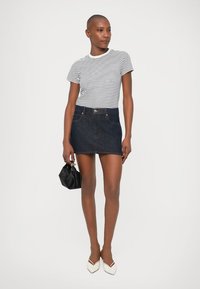 Tricou cu mânecă scurtă și dungi, asortat cu o fustă mini din denim închis, dotată cu închidere cu buton. Accesoriile includ o geantă mică neagră și pantofi albi.