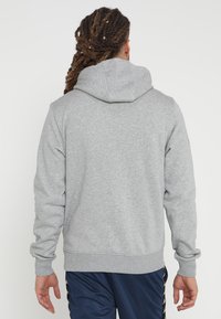 Sudadera gris con capucha ajustable, que ofrece un ajuste cómodo y puños y dobladillo acanalados, combinada con pantalones deportivos azul marino.