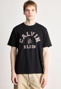 Črna bombažna majica s poudarjenim, kontrastnim natisnjenim logotipom, ki vključuje "CALVIN," "CK 1968," "NYC," in "KLEIN" v krepki pisavi.