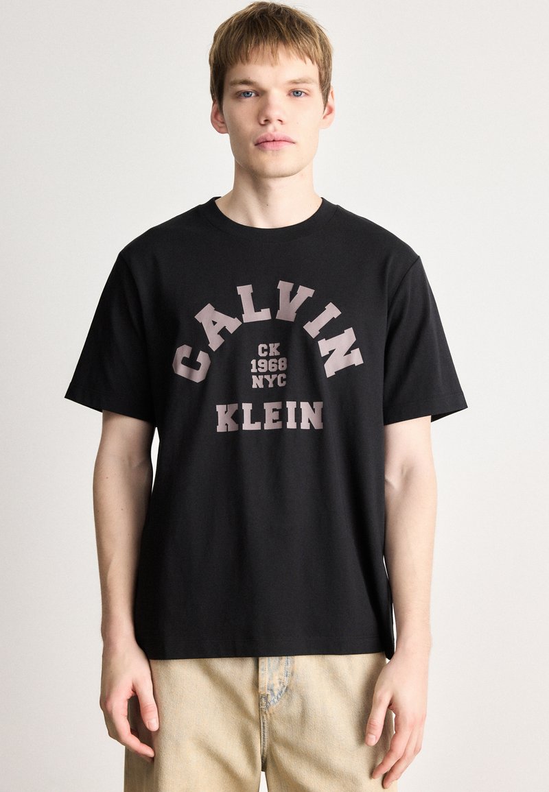 Črna bombažna majica s poudarjenim, kontrastnim natisnjenim logotipom, ki vključuje "CALVIN," "CK 1968," "NYC," in "KLEIN" v krepki pisavi.