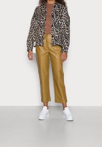 Veste à imprimé léopard, haut marron, pantalon en cuir jaune court, et baskets blanches à plateforme. Comprend des manches longues et une fermeture à boutons.