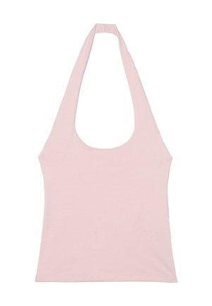 Femme portant un haut dos nu rose clair, un jean bleu clair à jambes larges et des tongs noires, debout avec une jambe levée contre un mur texturé.