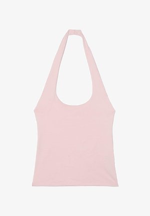 Femme portant un haut dos nu rose clair, un jean bleu clair à jambes larges et des tongs noires, debout avec une jambe levée contre un mur texturé.
