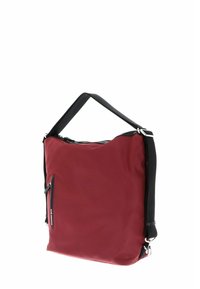 Sac en nylon rouge de forme carrée, avec une fermeture éclair en haut, une bandoulière noire et une poche zippée à l'avant pour plus de commodité.
