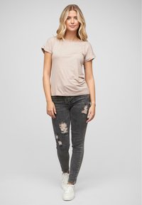 T-shirt beige à manches courtes associé à un jean skinny noir déchiré et des baskets blanches, présentant un design ajusté et une texture de tissu douce.