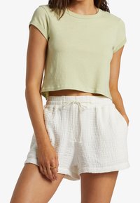 Jasnozielony, skrócony t-shirt z podwiniętymi rękawami, zestawiony z białymi, teksturowanymi szortami z elastyczną talią i sznurkiem.