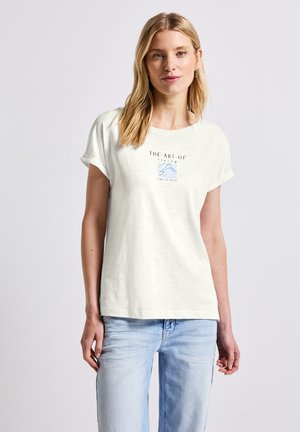 Light cream short-sleeve t-shirt with a relaxed fit. Features a printed square design in blue and gray, with the text "THE ART OF living."