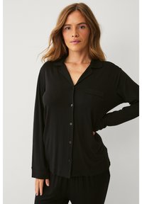 Haut de pyjama noir à manches longues en tissu lisse, avec un devant à boutons, un col et une poche poitrine, offrant une coupe décontractée.