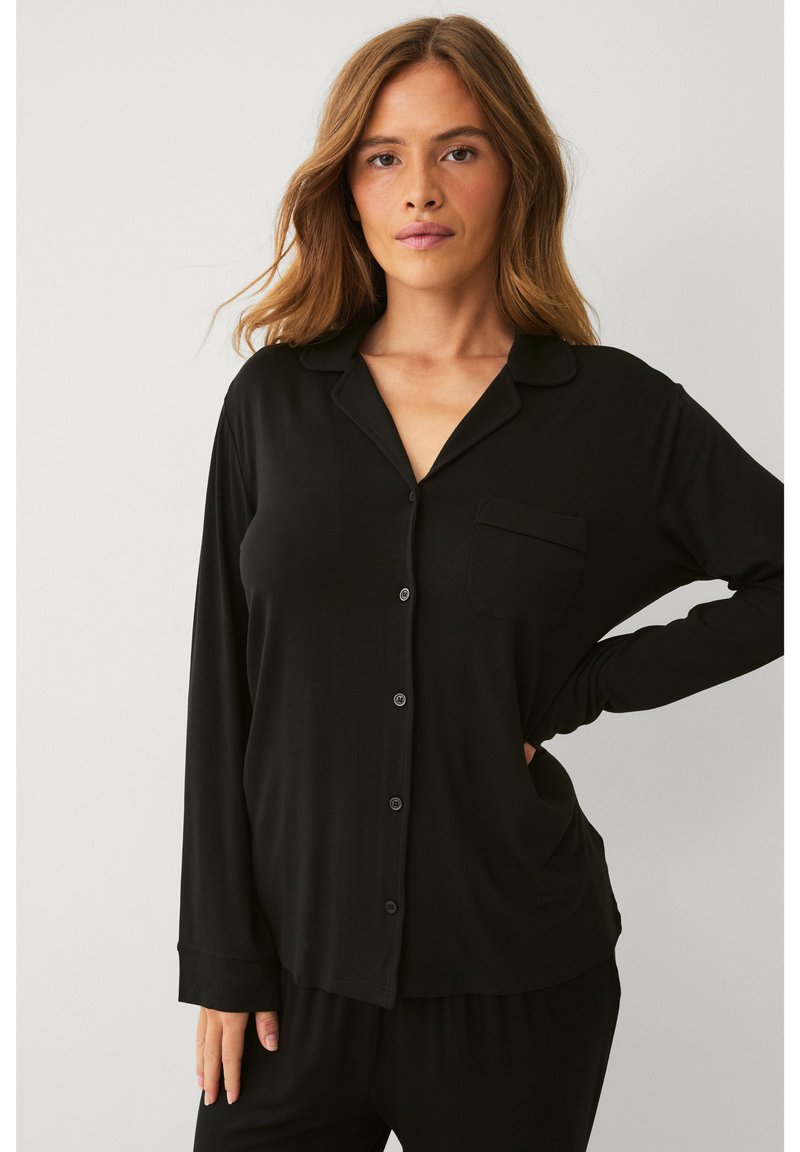Haut de pyjama noir à manches longues en tissu lisse, avec un devant à boutons, un col et une poche poitrine, offrant une coupe décontractée.