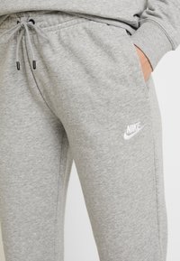 Grå sweatpants i mjukt material, med elastisk midjeband och dragsnöre, samt en vit Nike-logotyp på sidan.