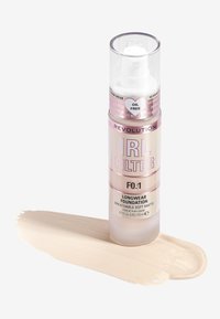 Fond de teint Revolution IRL Filter dans un flacon à pompe transparent avec des accents roses. Sur une surface, un échantillon de fond de teint beige clair au fini mat doux.