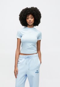 Jasnoniebieski krótki sportowy top z krótkimi rękawami, z małym logo. W zestawie z jasnoniebieskimi spodniami dresowymi z akcentami logo.