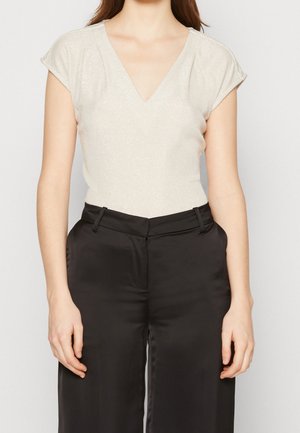 Mujer con una blusa de manga corta y escote en V de color beige claro combinada con pantalones negros de tiro alto y pernera ancha.