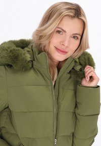 Geacă puffer verde măslin cu fermoar frontal, având glugă detasabilă cu blană și textură matlasată. Design pentru un plus de căldură și confort.