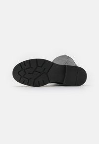 Suela de bota negra con patrón de goma texturizado. Presenta una punta redondeada y sección superior cosida, diseñada para ofrecer agarre y durabilidad.