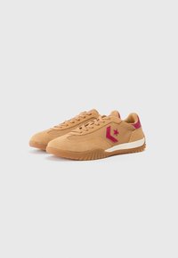 Zapatillas de ante beige con suelas de goma, con detalles en rosa y un logo de estrella. Diseño con cordones y patrones texturizados a lo largo de los lados.