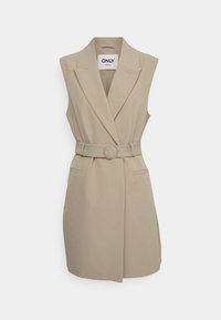 Beżowa sukienka marynarkowa bez rękawów z paskiem w talii ozdobionym okrągłą metalową klamrą, wyraźnymi klapami i dwoma bocznymi kieszeniami.