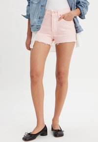 Shorts de mezclilla rosa claro con dobladillo deshilachado, diseño de cintura alta y estilo tradicional de cinco bolsillos, combinados con zapatos planos negros.