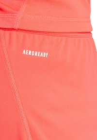 Korallfarbene Sportshorts aus atmungsaktivem Stoff. Zu den Merkmalen gehören ein elastischer Bund und ein weiß bedrucktes "AEROREADY"-Logo.