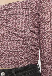 Top de manga longa em rosa claro com um padrão de estampas de leopardo escuras. Apresenta detalhes franzidos ao longo do corpo e das mangas, com uma silhueta ajustada.