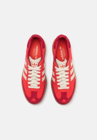 Czerwono-kremowe sneakersy wykonane z połączenia zamszu i siateczki, z klasycznymi trzema paskami po bokach oraz teksturowaną gumową podeszwą.