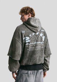 Gray oversized hoodie with a textured finish, featuring white printed text and stars on the back. Hooded design with dropped shoulders.