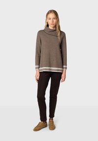Brauner, strukturierten Strickpullover mit weitem Kragen und gestreiftem Akzent am Saum, kombiniert mit dunkler Hose und braunen Wildledersneakern.