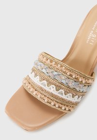 Sandale à talons beige avec des lanières décoratives ornées d'accents dorés, bleus, en perle et de sequins; design à bout carré lisse.