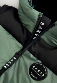 Grüne und schwarze Pufferjacke mit Reißverschluss, strukturiertem Stoff, rundem Logopatch und kontrastierenden Farbblöcken.