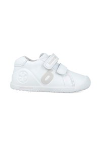 Zapatos blancos para niños con un upper sintético liso, dos correas ajustables de Velcro, puntera redondeada y un logo circular en el talón.