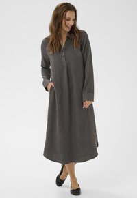 Abito lungo di un grigio scuro, realizzato in un tessuto texturizzato, con colletto, zip frontale e tasche laterali. Accentuato da maniche lunghe.