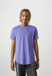Korte mouwen, ronde hals t-shirt van lichtpaarse stof, met een gebogen zoom en een gladde textuur. Gemaakt met donkere grijze jeans.
