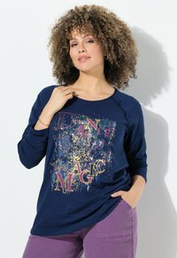 Camicia a maniche lunghe blu navy con una grafica colorata "DANCE MAGIC" in oro e viola, abbinata a pantaloni viola. Tessuto morbido e texturizzato.