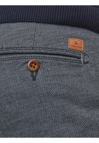 Mörkblått texturerat tyg med ett fiskbensmönster, med en brun knapp och en läderetikett som säger "JACK & JONES."