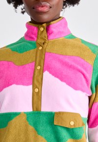 Maglione in pile con motivi ondulati multicolori in rosa, verde e beige, caratterizzato da un collo alto e bottoni a pressione, con una tasca sul petto.