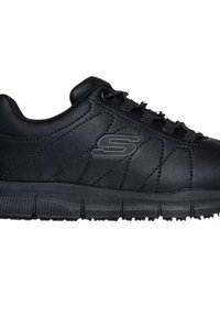 Zapatilla deportiva baja negra con suela texturizada, costuras decorativas, parte delantera con cordones y un logotipo en relieve de "S" en el lateral.