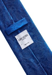 Blå mönstrad slips med paisleymönster, tillverkad av strukturerad tyg. Inkluderar en vit etikett med varumärkesnamn och ursprungsinformation.