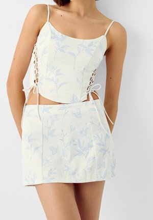 Set composto da un crop top bianco e una mini gonna con motivi floreali blu chiaro, caratterizzato da lacci laterali e dettagli con fiocchi in vita.