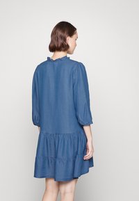 Robe en jean avec un décolleté volanté, des manches trois-quarts et une jupe à volants, le tout dans une couleur bleue médium unie.