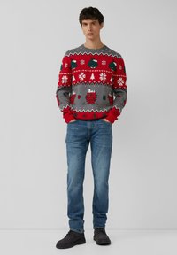 Czerwono-szary sweter na drutach z motywami świątecznymi, w tym prezentami i płatkami śniegu. Zestawiony z niebieskimi dżinsami i czarnymi butami.